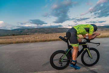 Image showing Triathlete riding his bicycle during sunset, preparing for a marathon. The warm colors of the sky provide a beautiful backdrop for his determined and focused effort.