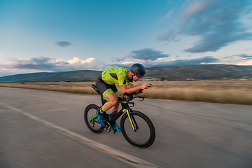 Image showing Triathlete riding his bicycle during sunset, preparing for a marathon. The warm colors of the sky provide a beautiful backdrop for his determined and focused effort.