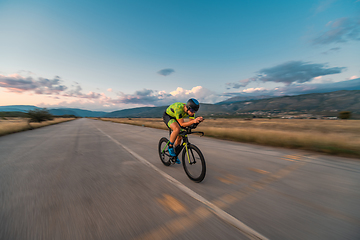 Image showing Triathlete riding his bicycle during sunset, preparing for a marathon. The warm colors of the sky provide a beautiful backdrop for his determined and focused effort.