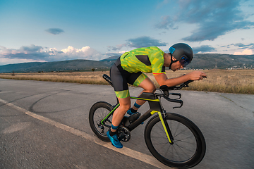 Image showing Triathlete riding his bicycle during sunset, preparing for a marathon. The warm colors of the sky provide a beautiful backdrop for his determined and focused effort.