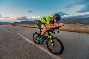 Image showing Triathlete riding his bicycle during sunset, preparing for a marathon. The warm colors of the sky provide a beautiful backdrop for his determined and focused effort.