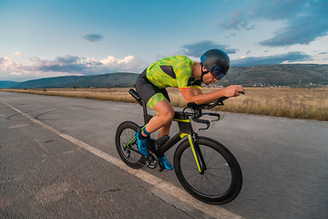 Image showing Triathlete riding his bicycle during sunset, preparing for a marathon. The warm colors of the sky provide a beautiful backdrop for his determined and focused effort.