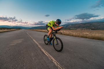 Image showing Triathlete riding his bicycle during sunset, preparing for a marathon. The warm colors of the sky provide a beautiful backdrop for his determined and focused effort.