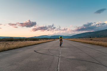 Image showing Triathlete riding his bicycle during sunset, preparing for a marathon. The warm colors of the sky provide a beautiful backdrop for his determined and focused effort.