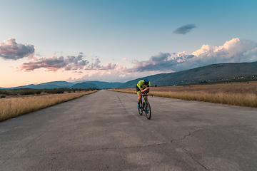 Image showing Triathlete riding his bicycle during sunset, preparing for a marathon. The warm colors of the sky provide a beautiful backdrop for his determined and focused effort.