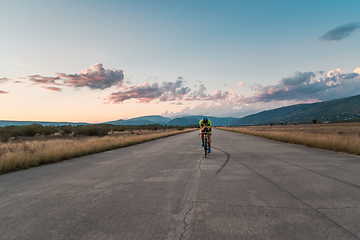 Image showing Triathlete riding his bicycle during sunset, preparing for a marathon. The warm colors of the sky provide a beautiful backdrop for his determined and focused effort.