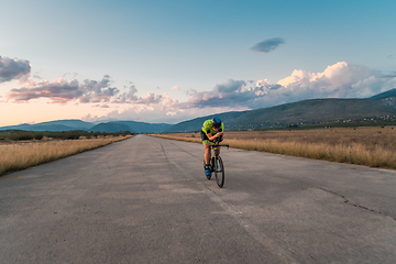 Image showing Triathlete riding his bicycle during sunset, preparing for a marathon. The warm colors of the sky provide a beautiful backdrop for his determined and focused effort.