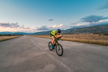 Image showing Triathlete riding his bicycle during sunset, preparing for a marathon. The warm colors of the sky provide a beautiful backdrop for his determined and focused effort.