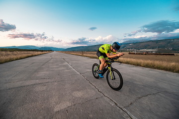 Image showing Triathlete riding his bicycle during sunset, preparing for a marathon. The warm colors of the sky provide a beautiful backdrop for his determined and focused effort.