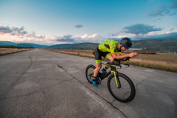 Image showing Triathlete riding his bicycle during sunset, preparing for a marathon. The warm colors of the sky provide a beautiful backdrop for his determined and focused effort.