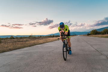 Image showing Triathlete riding his bicycle during sunset, preparing for a marathon. The warm colors of the sky provide a beautiful backdrop for his determined and focused effort.