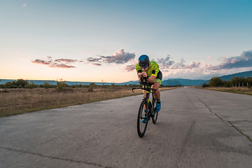 Image showing Triathlete riding his bicycle during sunset, preparing for a marathon. The warm colors of the sky provide a beautiful backdrop for his determined and focused effort.