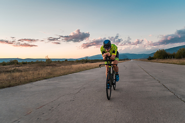 Image showing Triathlete riding his bicycle during sunset, preparing for a marathon. The warm colors of the sky provide a beautiful backdrop for his determined and focused effort.