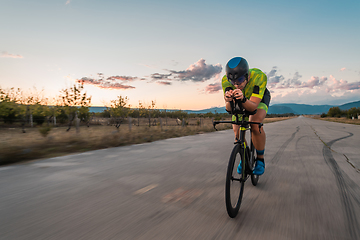 Image showing Triathlete riding his bicycle during sunset, preparing for a marathon. The warm colors of the sky provide a beautiful backdrop for his determined and focused effort.