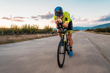 Image showing Triathlete riding his bicycle during sunset, preparing for a marathon. The warm colors of the sky provide a beautiful backdrop for his determined and focused effort.