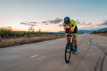 Image showing Triathlete riding his bicycle during sunset, preparing for a marathon. The warm colors of the sky provide a beautiful backdrop for his determined and focused effort.