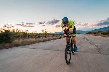 Image showing Triathlete riding his bicycle during sunset, preparing for a marathon. The warm colors of the sky provide a beautiful backdrop for his determined and focused effort.