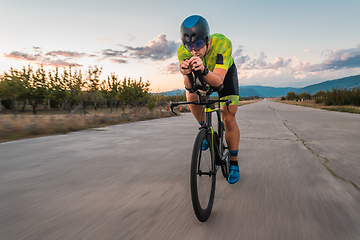 Image showing Triathlete riding his bicycle during sunset, preparing for a marathon. The warm colors of the sky provide a beautiful backdrop for his determined and focused effort.