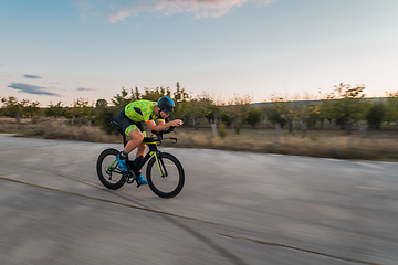 Image showing Triathlete riding his bicycle during sunset, preparing for a marathon. The warm colors of the sky provide a beautiful backdrop for his determined and focused effort.