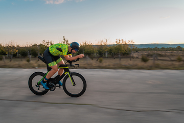 Image showing Triathlete riding his bicycle during sunset, preparing for a marathon. The warm colors of the sky provide a beautiful backdrop for his determined and focused effort.