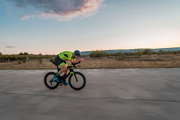 Image showing Triathlete riding his bicycle during sunset, preparing for a marathon. The warm colors of the sky provide a beautiful backdrop for his determined and focused effort.