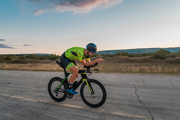 Image showing Triathlete riding his bicycle during sunset, preparing for a marathon. The warm colors of the sky provide a beautiful backdrop for his determined and focused effort.