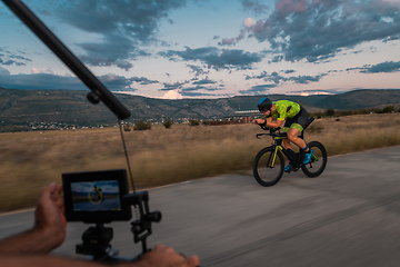 Image showing A videographer recording a triathlete riding his bike preparing for an upcoming marathon.Athlete's physical endurance and the dedication required to succeed in the sport.