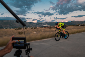 Image showing A videographer recording a triathlete riding his bike preparing for an upcoming marathon.Athlete's physical endurance and the dedication required to succeed in the sport.