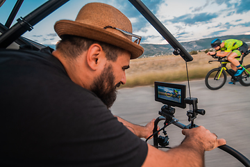 Image showing A videographer recording a triathlete riding his bike preparing for an upcoming marathon.Athlete's physical endurance and the dedication required to succeed in the sport.