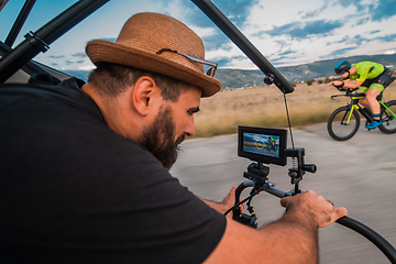 Image showing A videographer recording a triathlete riding his bike preparing for an upcoming marathon.Athlete's physical endurance and the dedication required to succeed in the sport.