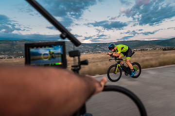 Image showing A videographer recording a triathlete riding his bike preparing for an upcoming marathon.Athlete's physical endurance and the dedication required to succeed in the sport.