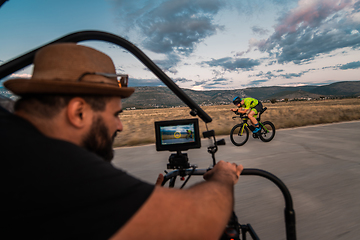 Image showing A videographer recording a triathlete riding his bike preparing for an upcoming marathon.Athlete's physical endurance and the dedication required to succeed in the sport.