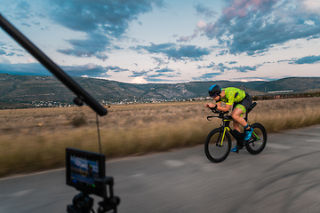 Image showing A videographer recording a triathlete riding his bike preparing for an upcoming marathon.Athlete's physical endurance and the dedication required to succeed in the sport.