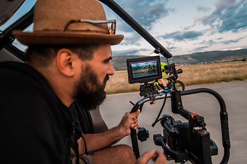 Image showing A videographer recording a triathlete riding his bike preparing for an upcoming marathon.Athlete's physical endurance and the dedication required to succeed in the sport.