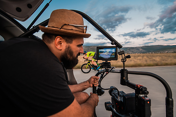 Image showing A videographer recording a triathlete riding his bike preparing for an upcoming marathon.Athlete's physical endurance and the dedication required to succeed in the sport.