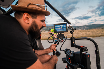 Image showing A videographer recording a triathlete riding his bike preparing for an upcoming marathon.Athlete's physical endurance and the dedication required to succeed in the sport.