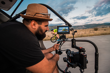 Image showing A videographer recording a triathlete riding his bike preparing for an upcoming marathon.Athlete's physical endurance and the dedication required to succeed in the sport.