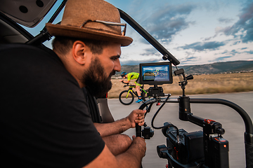 Image showing A videographer recording a triathlete riding his bike preparing for an upcoming marathon.Athlete's physical endurance and the dedication required to succeed in the sport.