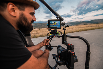 Image showing A videographer recording a triathlete riding his bike preparing for an upcoming marathon.Athlete's physical endurance and the dedication required to succeed in the sport.