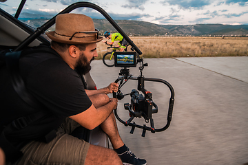 Image showing A videographer recording a triathlete riding his bike preparing for an upcoming marathon.Athlete's physical endurance and the dedication required to succeed in the sport.