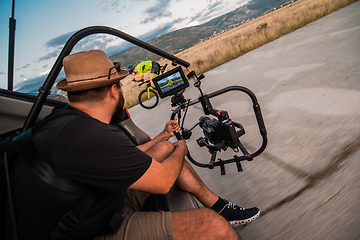 Image showing A videographer recording a triathlete riding his bike preparing for an upcoming marathon.Athlete's physical endurance and the dedication required to succeed in the sport.