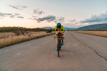 Image showing Triathlete riding his bicycle during sunset, preparing for a marathon. The warm colors of the sky provide a beautiful backdrop for his determined and focused effort.