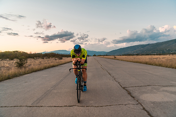 Image showing Triathlete riding his bicycle during sunset, preparing for a marathon. The warm colors of the sky provide a beautiful backdrop for his determined and focused effort.