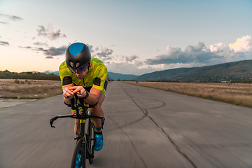 Image showing Triathlete riding his bicycle during sunset, preparing for a marathon. The warm colors of the sky provide a beautiful backdrop for his determined and focused effort.