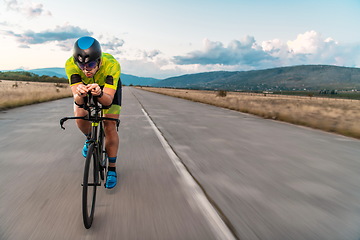 Image showing Triathlete riding his bicycle during sunset, preparing for a marathon. The warm colors of the sky provide a beautiful backdrop for his determined and focused effort.