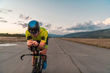 Image showing Triathlete riding his bicycle during sunset, preparing for a marathon. The warm colors of the sky provide a beautiful backdrop for his determined and focused effort.