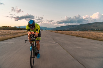 Image showing Triathlete riding his bicycle during sunset, preparing for a marathon. The warm colors of the sky provide a beautiful backdrop for his determined and focused effort.