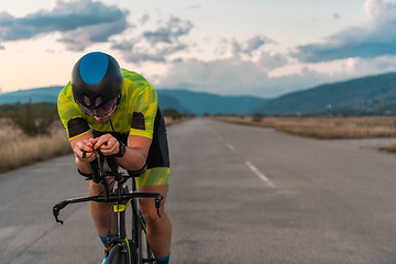 Image showing Triathlete riding his bicycle during sunset, preparing for a marathon. The warm colors of the sky provide a beautiful backdrop for his determined and focused effort.