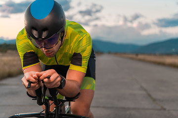 Image showing Close up photo of triathlete riding his bicycle during sunset, preparing for a marathon. The warm colors of the sky provide a beautiful backdrop for his determined and focused effort.