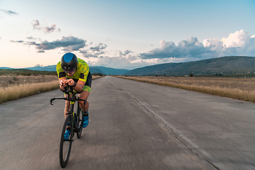 Image showing Triathlete riding his bicycle during sunset, preparing for a marathon. The warm colors of the sky provide a beautiful backdrop for his determined and focused effort.